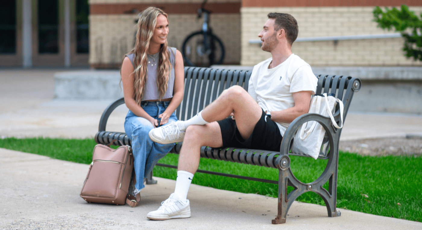 A college-age girl and boy sitting on a bench 